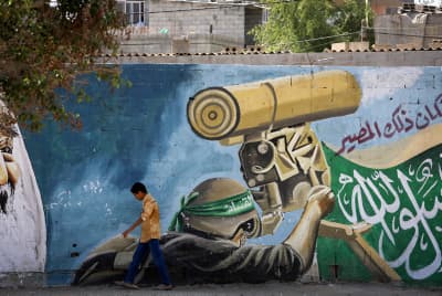 A Palestinian boy walks past a mural depicting a masked fighter of the Qassam Brigades, the armed wing of Hamas. Rafah, southern Gaza Strip.