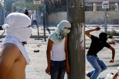 Masked Palestinian protesters throw stones towards Israeli police